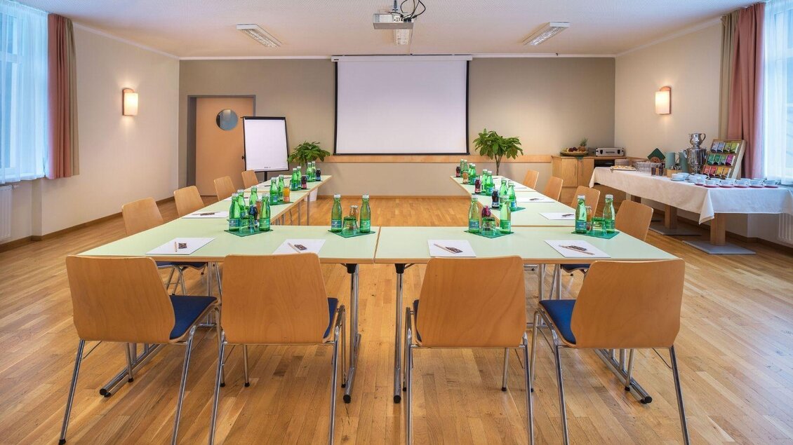 Ein modernes Konferenzzimmer mit einem großen Tisch und Stühlen. Auf dem Tisch stehen Wasserflaschen und das Zimmer ist gut beleuchtet. | © JUFA Hotels