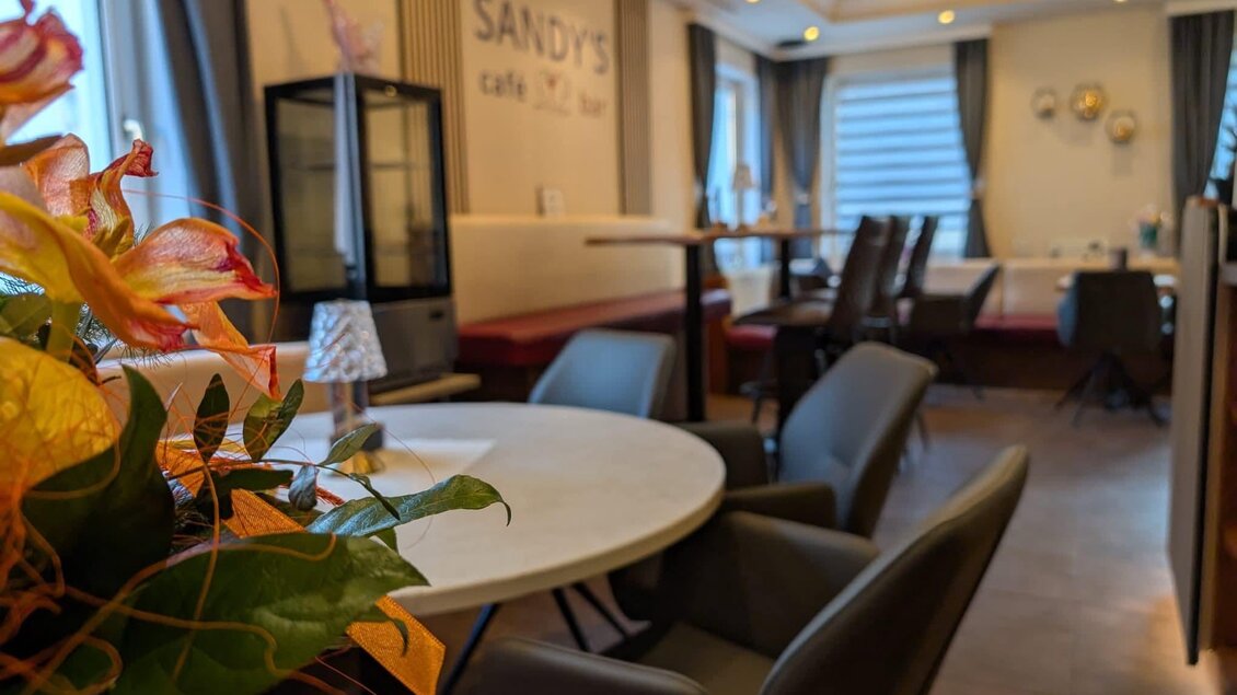Ein gemütliches Café mit modernen Tischen und Stühlen. Die freundliche Atmosphäre wird durch Pflanzen und dezentes Licht unterstützt. | © Sandy`s Café Bar