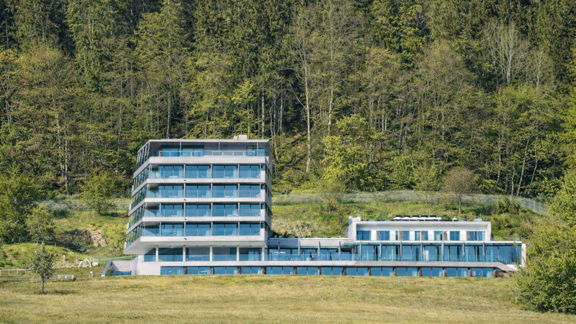 Ein modernes Hotelgebäude umgeben von Grünflächen und Wälder. Die Architektur ist klar und offen mit großen Fenstern. | © Tauroa GmbH
