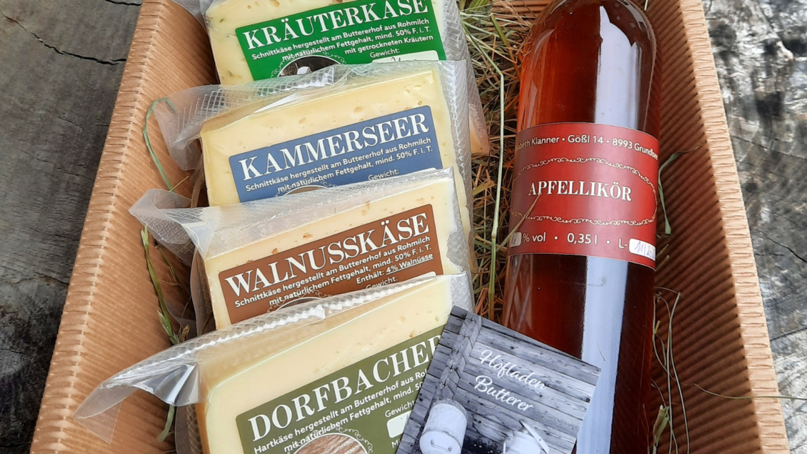 Eine Auswahl an Käse mit verschiedenen Sorten und einem Fläschchen Apfel-Likör. Die Produkte sind in einem Korb mit grünem Heu arrangiert. | © Butterer Hofladen
