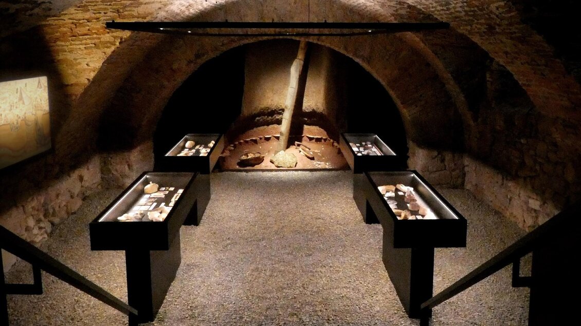 Gewölbter Kellerraum der Ausstellung Stein.Zeit. im Stift Rein mit beleuchteten Vitrinen und archäologischen Steinzeitfunden. | © Stift Rein
