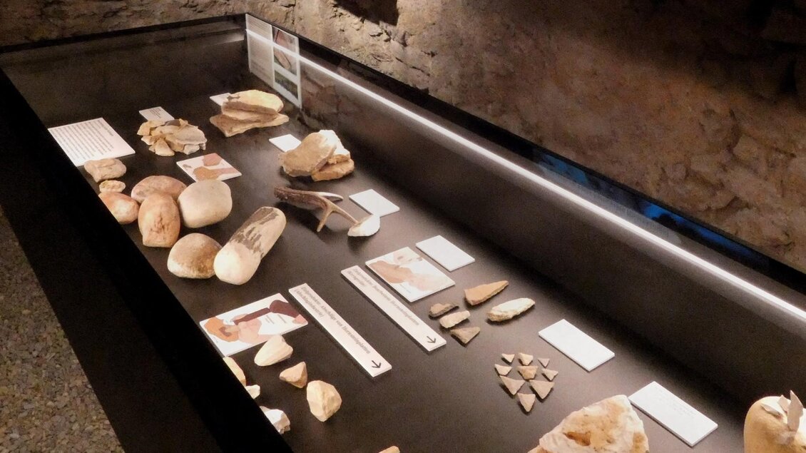 Beleuchtete Museumsvitrine der Ausstellung Stein.Zeit. im Stift Rein mit steinzeitlichen Werkzeugen, Knochen und Fundstücken. | © Stift Rein