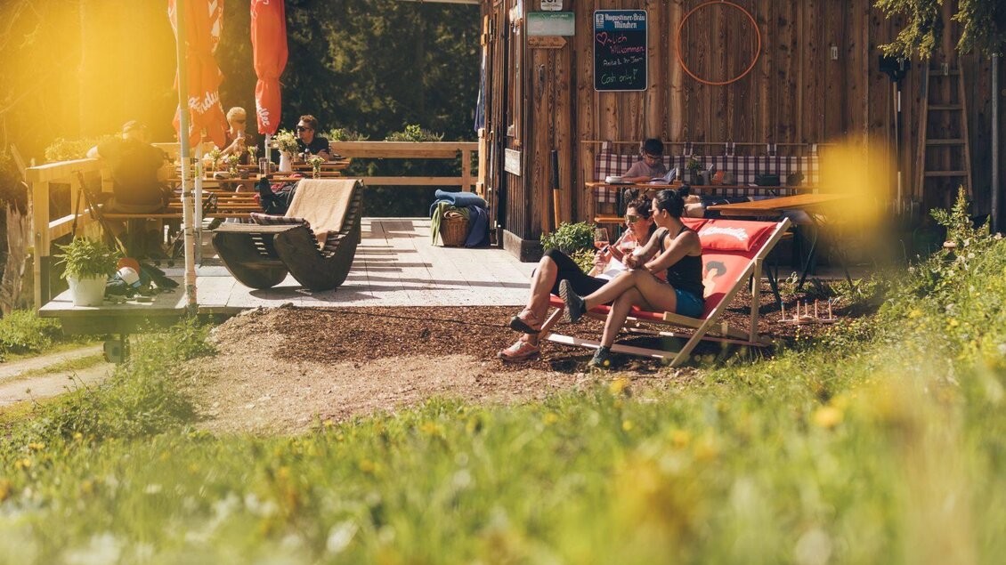 <p>Eine gemütliche Terrasse mit Sonnenliegen und Gästen, die sich entspannen. Im Hintergrund steht ein Stellenkogelhütte, umgeben von einer grünen Wiese.</p> | © Krewenka