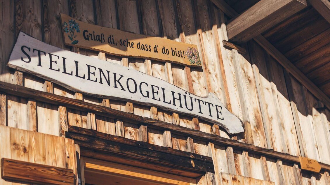 <p>Eine Hütte mit dem Schild "Stellenkogelhütte". Oben hängt ein weiteres Schild mit der Begrüßung "Griaß di, sche dass d’ do bist!".</p> | © Krewenka