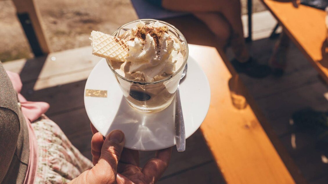 <p>Ein guter Kaffe mit Schlagobers und Waffel in einem Glas. Dieser wird auf deinem weißten Teller auf die Terrasse der Stellenkogelhütte serviert.</p> | © Krewenka