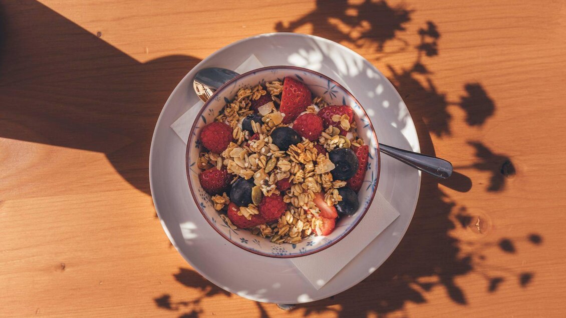 <p>Zum Frühstück gibt es in einerSchüssel Müsli mit frischen Beeren. Der Schatten von Pflanzen zeichnet interessante Muster auf die Oberfläche auf den Holztisch vor der Stellenkogelhütte.</p> | © Krewenka