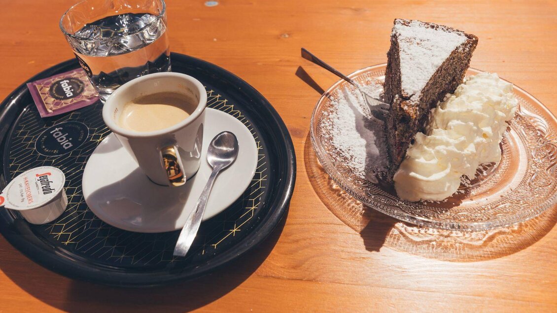 <p>Eine Tasse Kaffee mit Wasser auf einem Tablett. Dazu wird ein Stück Schokoladentorte und Schlagobers auf der Terrasse der Stellenkogelhütte serviert. </p> | © Krewenka