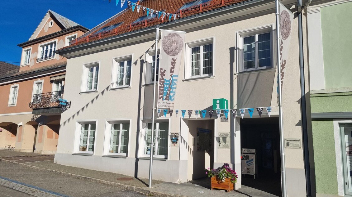 Ein Gebäude mit bunten Fahnen und einem einladenden Eingang. Die Fassade ist hell und freundlich, umgeben von einem klaren blauen Himmel. | © Tanja Beren
