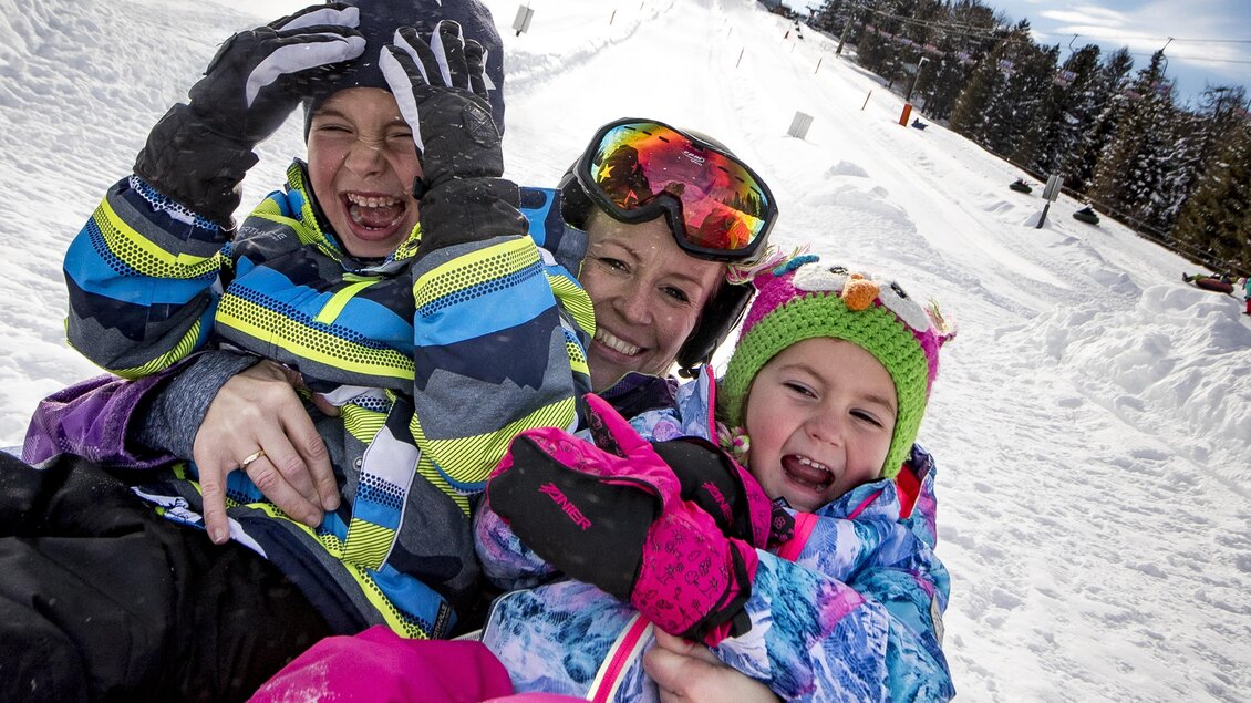 Eine fröhliche Familie hat Spaß beim Schlittenfahren im Schnee. Die Kinder lachen und tragen bunte Winterkleidung. | © Murtal Seilbahnen Betriebs GmbH