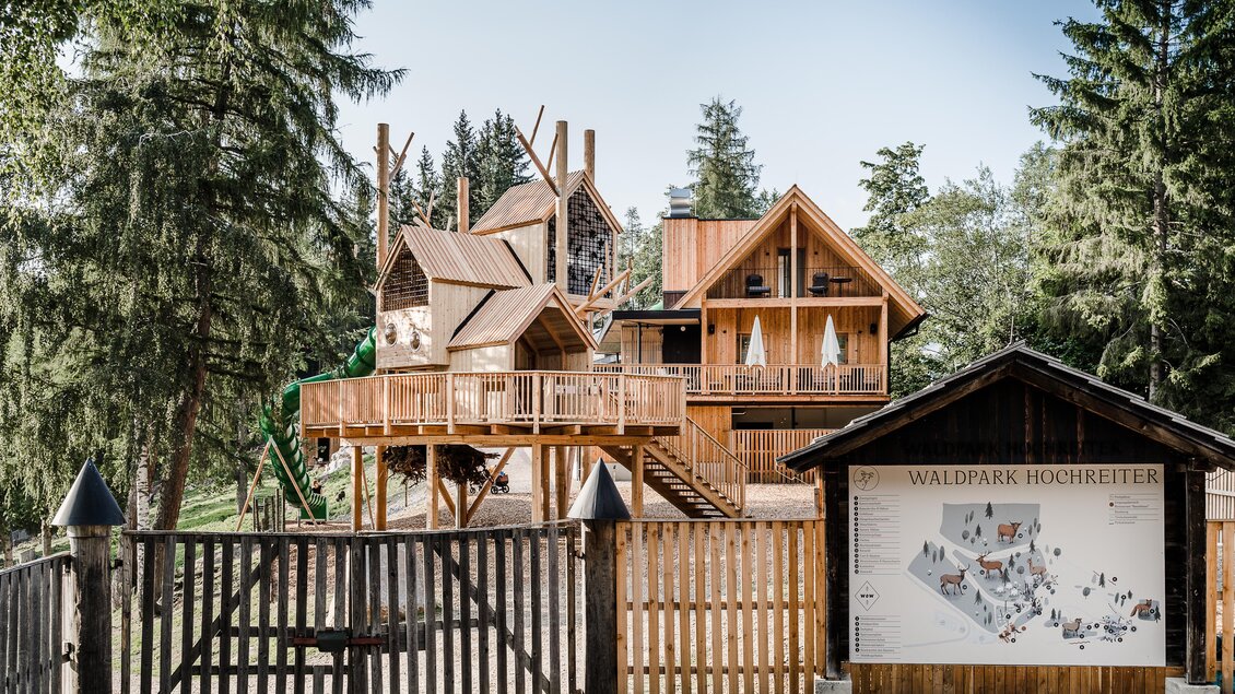 Ein Holzhaus im Wald, das modern und einladend aussieht. Neben dem Gebäude steht ein Informationsschild zum Waldpark Hochreiter. | © Waldpark Hochreiter