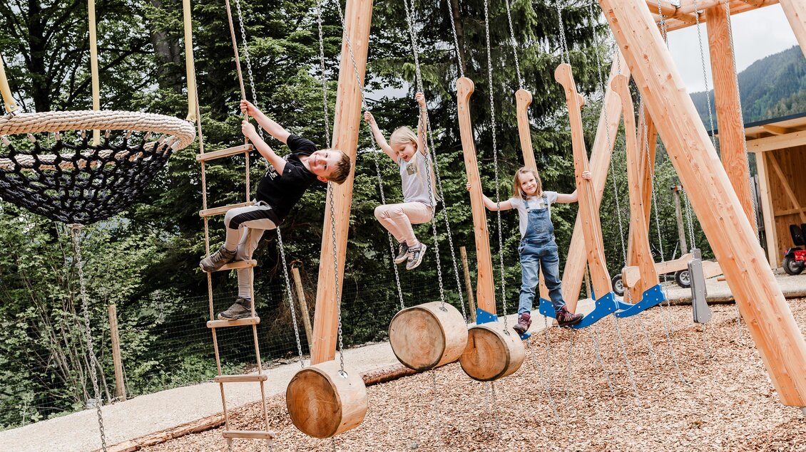 Ein Spielplatz mit Kindern, die an Schaukeln und Kletterelementen spielen. Die Umgebung ist naturnah, umgeben von Bäumen und einem ruhigen Hintergrund. | © Waldpark Hochreiter