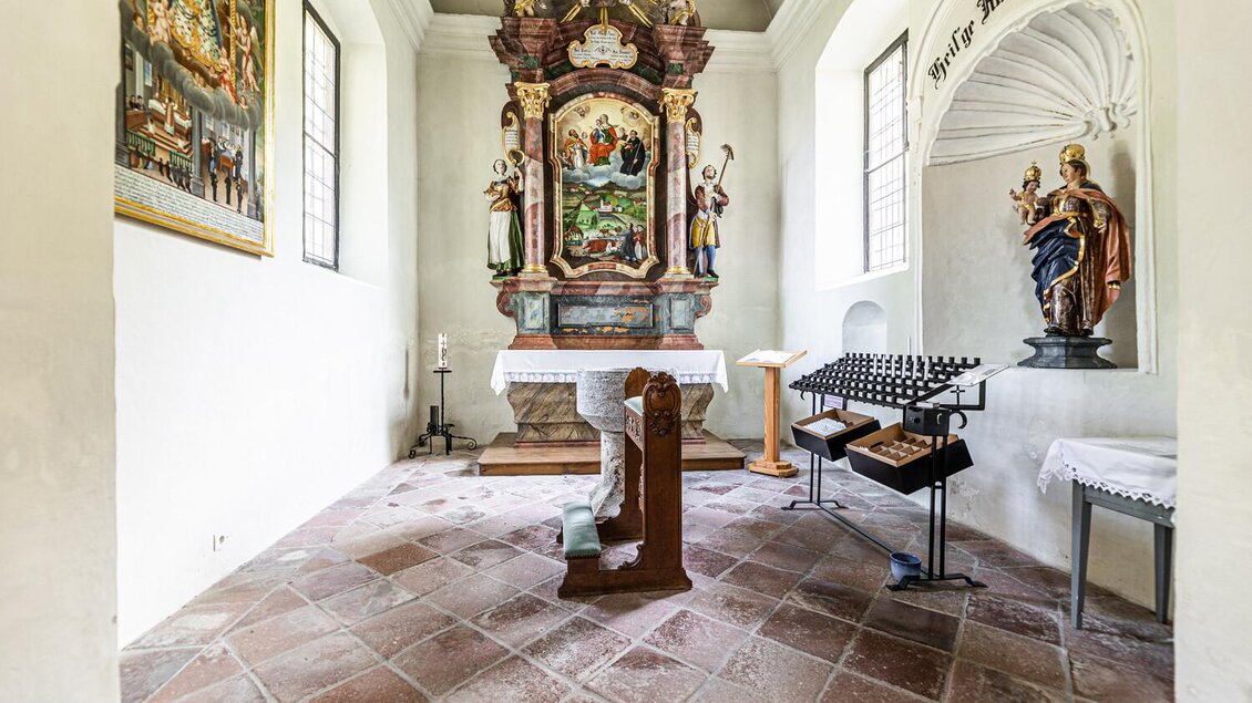 Ein Innenraum einer Kirche mit einer beeindruckenden Altaranlage und gestuften Fenstern. Rechts steht eine Statue und auf einem Tisch liegt ein Kranz aus Kerzen. | © TV Gesäuse