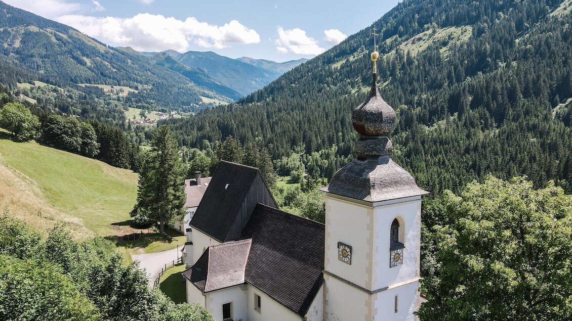 Eine malerische Kirche inmitten von grünen Bergen und Wäldern. Der Himmel ist klar und die Landschaft ist friedlich. | © TV Gesäuse