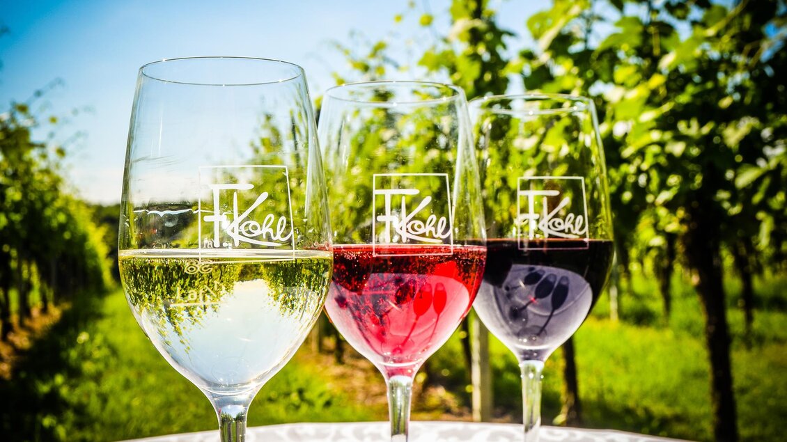 Drei Gläser Wein stehen vor einem Weinberg. Das erste Glas enthält weißen Wein, das zweite roséfarbene und das dritte roten Wein. | © Arthur Michalek