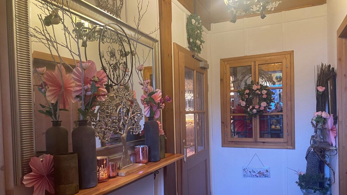 Ein einladender Flur mit einer dekorativen Spiegelwand und einer Holzablage. Blumenarrangements und eine Wandschmuck verleihen dem Raum eine warme Atmosphäre. | © Bettina Scheck