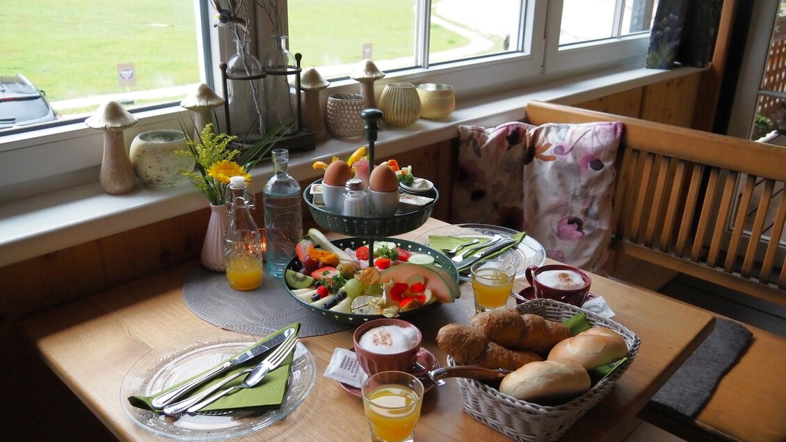 Ein schön gedeckter Tisch mit frischem Frühstück. Es gibt Brötchen, Obst, Eier und Getränke in einem einladenden Ambiente.