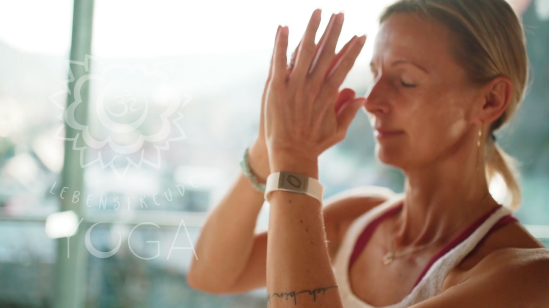 Eine Frau macht Yoga in einem hellen Raum mit Blick auf die Natur. Sie meditiert mit geschlossenen Augen und gefalteten Händen. | © Tourismusverband Murau