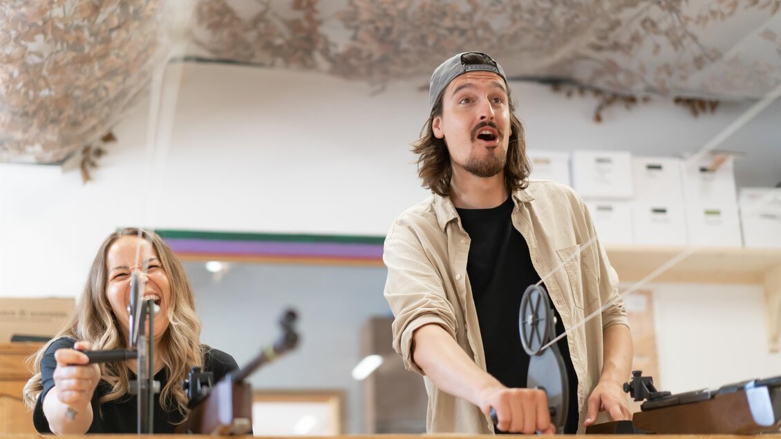 Zwei Personen stehen an einem Tisch in einem Geschäft. Sie lachen und scheinen Spaß zu haben, während sie an einem Projekt arbeiten. | © www.zloam.at