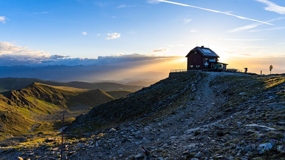 Ein altes Haus steht auf einem Hügel mit Blick auf ein weites, hügeliges Landschaftsbild. Der Sonnenuntergang taucht die Szene in warmes Licht. | © Christoph Trois
