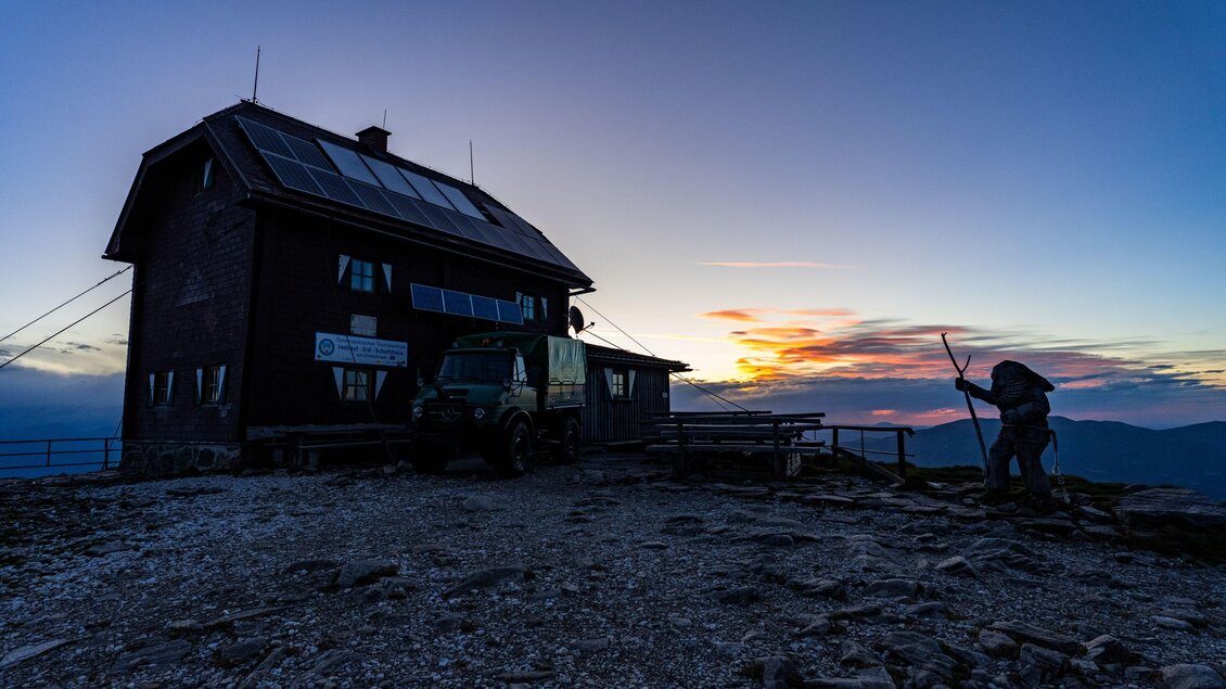 Ein Berghaus bei Sonnenuntergang, umgeben von felsigem Terrain. Sanfte Farben am Himmel schaffen eine ruhige Atmosphäre. | © Christoph Trois