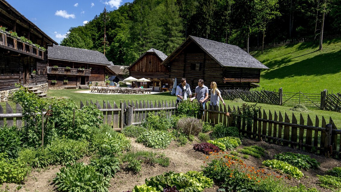 Bauerngarten von einst mit Gemüse und Kräuter im Freilichtmuseum Stübing, drei Personen stehen am Holz-Gartenzaun.  | © Region Graz-Tom Lamm