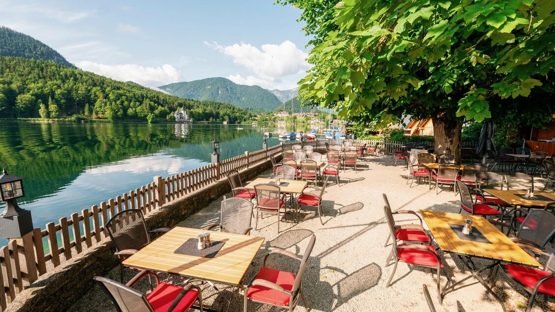 Eine schöne Terrasse am Wasser mit Tischen und Stühlen. Im Hintergrund sind Berge und ein klarer blauer Himmel zu sehen. | © Karl Steinegger Fotografie