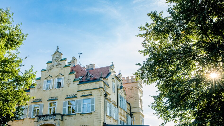 Schloss Lustbühel mit Türmen und Bäumen bei strahlendem Himmel in Graz.