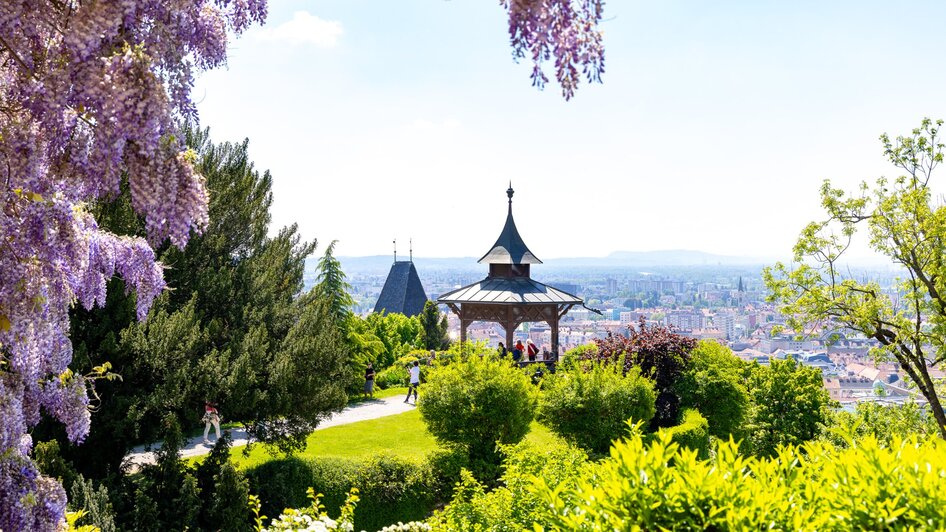 Blick vom Schlossberg auf Graz mit blühenden Bäumen.