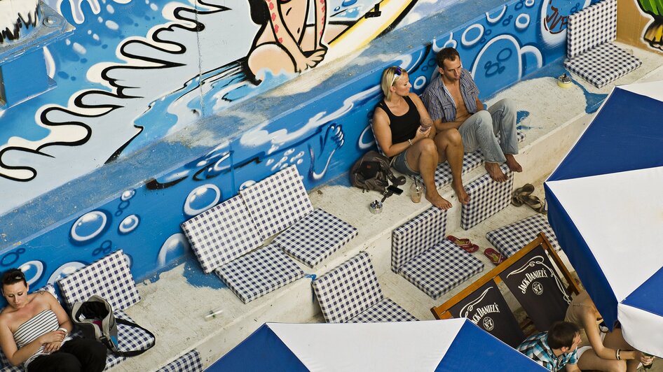 Blick auf eine Strandbar mit Graffiti und Sonnenliegen.