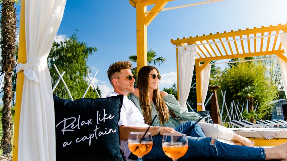 Paar entspannt in einer Lounge mit Cocktails und einer Kissenbotschaft.