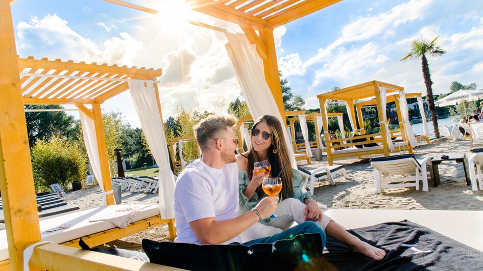 Ein Paar genießt Cocktails in einer Strandlounge mit Sonnenschein.