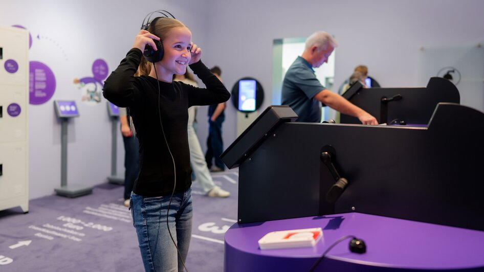Ein lächelnder Teenager trägt Kopfhörer und erkundet interaktive Displays im Museum. | © Stellework