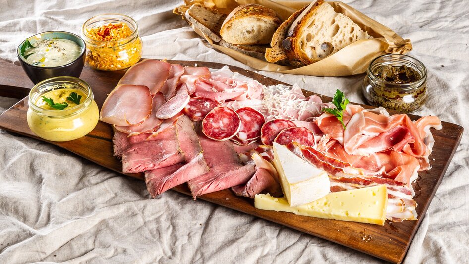 Platte mit Wurst, Käse, Dips und Brot auf einem Tisch.