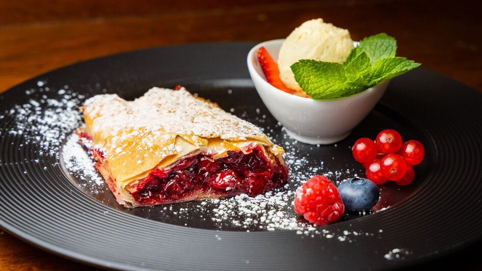 Ein köstlicher Kirschstrudel mit Eis und Beeren auf einem Teller.