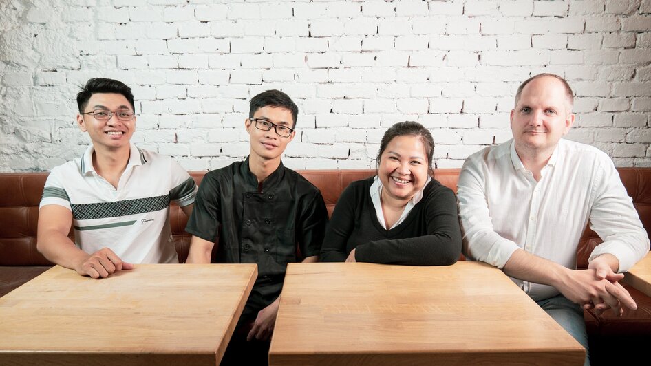 Vier Personen sitzen an einem Tisch in einem Restaurant mit Backsteinmauer.
