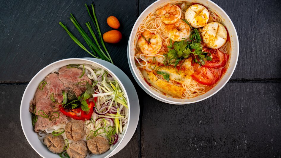 Zwei Schalen mit Nudelsuppe, eine mit Fleischbällchen und die andere mit Shrimps.