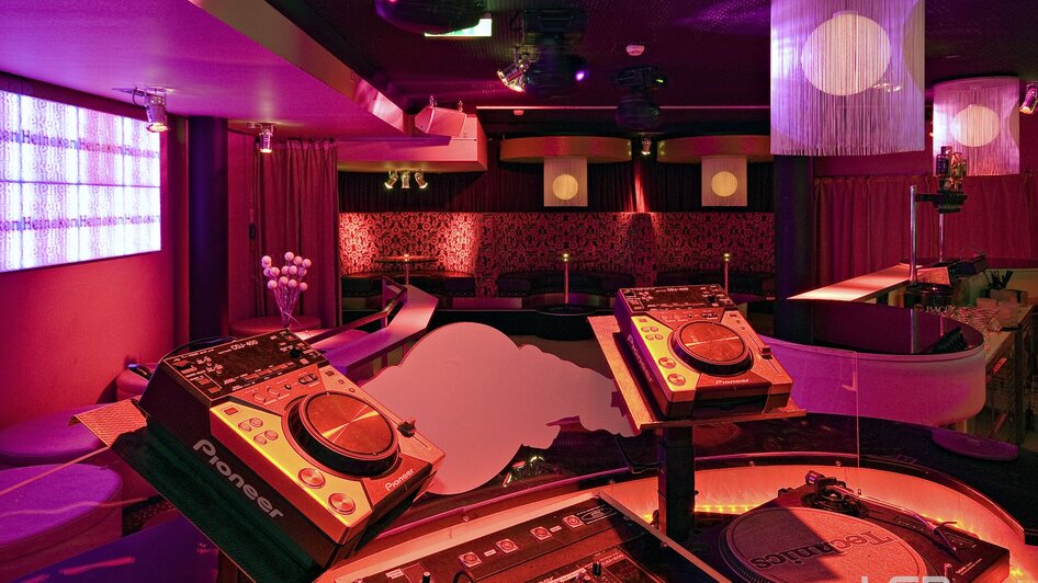 Einblick in einen stilvollen Club mit DJ-Equipment und bunten Lichtern.