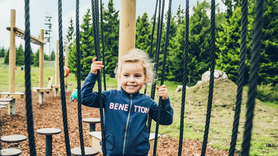 Ein Mädchen spielt fröhlich auf einem Spielplatz mit Seilen. | © Lupi Spuma
