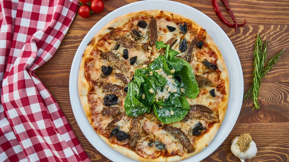 Leckere Pizza mit Spinat, Oliven und getrockneten Tomaten auf einem Holzuntergrund.
