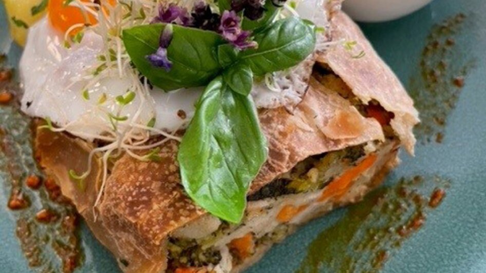 Vegetarischer Gemüse-Strudel mit Spiegelei, Beilagen und Kräutern auf einem Teller.