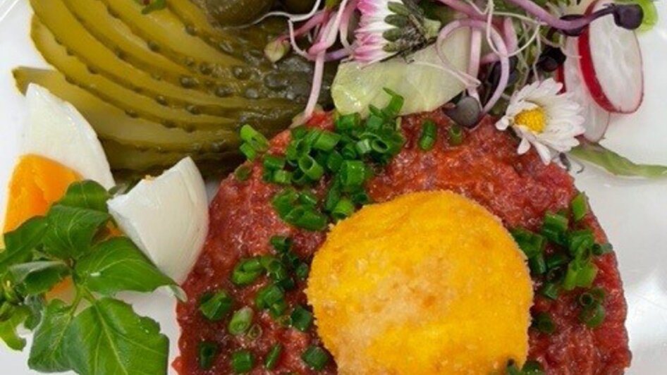 Detailansicht eines kulinarischen Gerichts mit Beef Tartar und Beilagen wie Gurken und Kräuter.