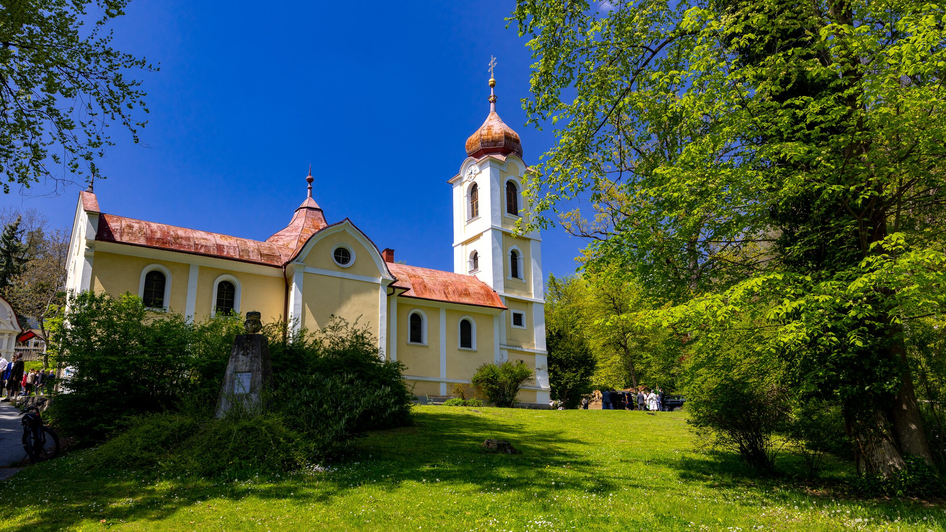 Eine gelbe Kirche mit einer roten Kuppel und umgebendem Grün am Rosenhain in Graz.
