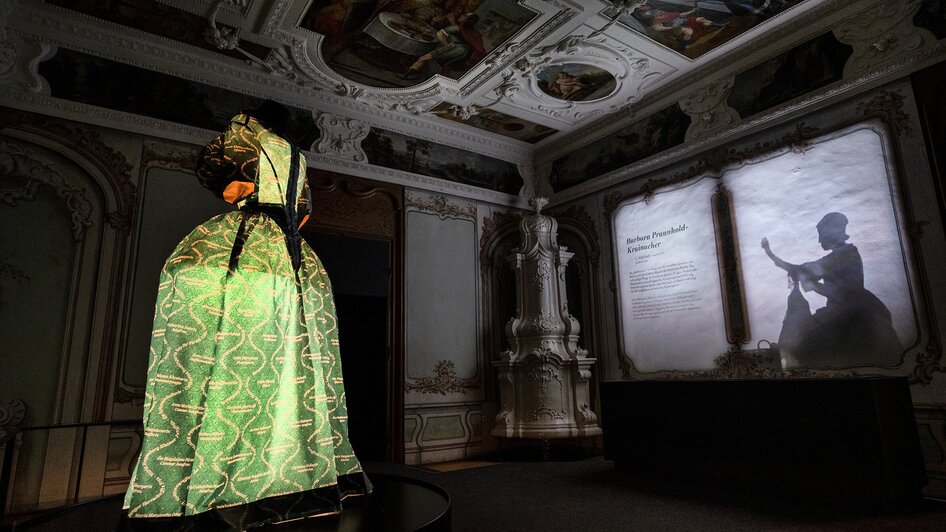 Beleuchtetes Kleid in einem historischen Raum mit projizierten Schatten.