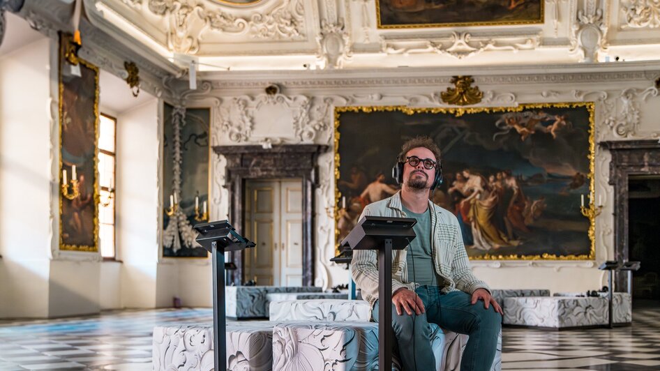 Mann mit Kopfhörern sitzt in einem kunstvollen Raum.