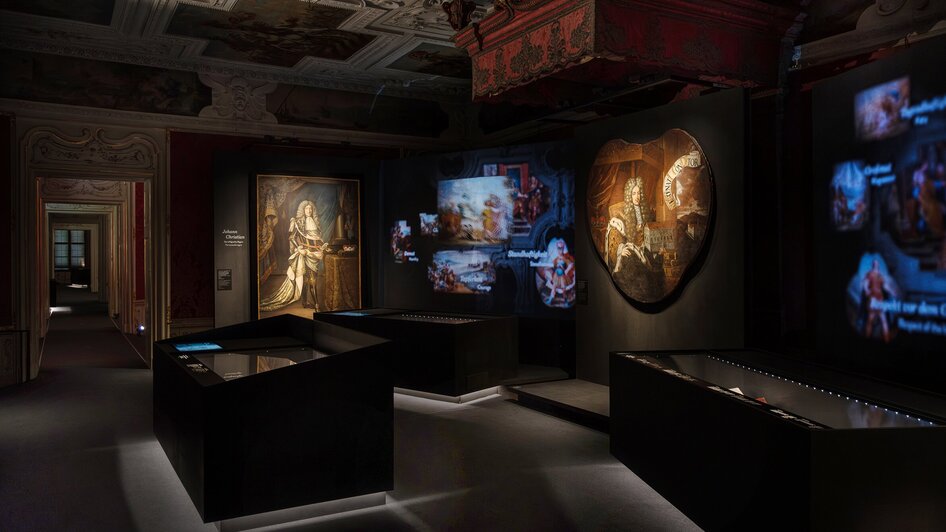 Dunkler Ausstellungsraum mit Kunstwerken und digitaler Projektion.
