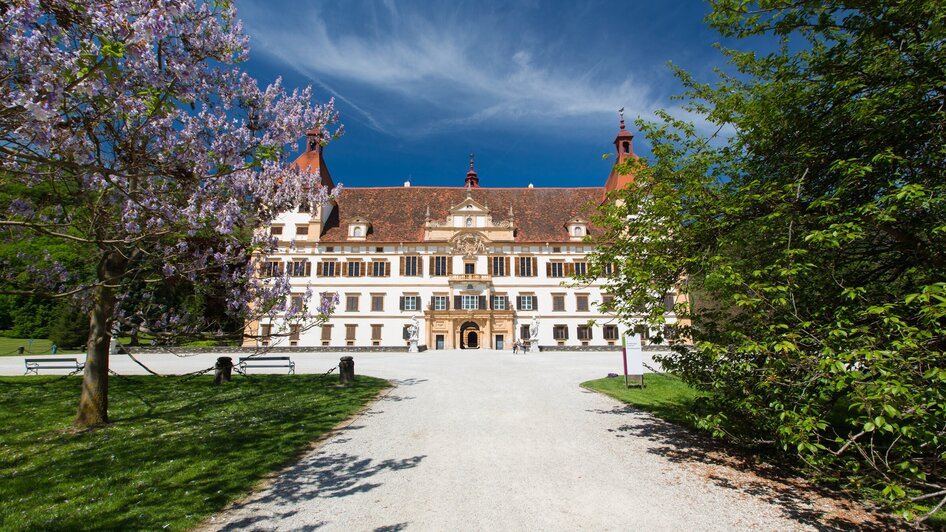 Schloss Eggenberg in Graz, umgeben von blühenden Bäumen und klarem Himmel.