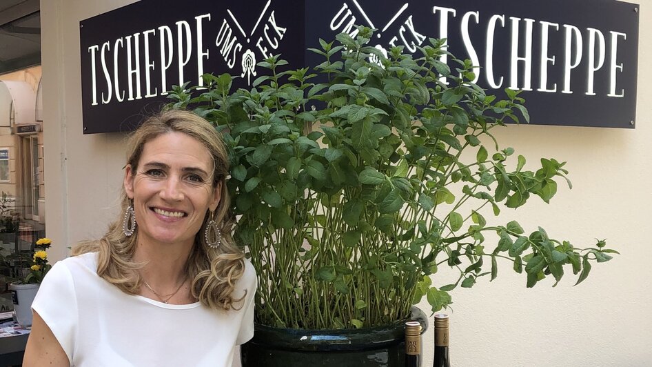 Eine freundliche Frau neben einem großen Topf mit frischen Kräutern bei Tscheppe.