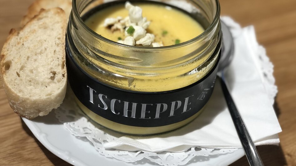 Eine cremige Suppe in einem Glas mit Brot, Popcorn und einem Löffel.