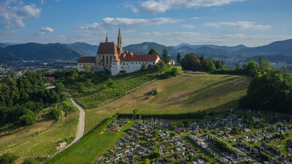 Luftaufnahme der Wallfahrtskirche Maria Strassengel mit einem Friedhof im Vordergrund. | © TV Region Graz - PicFly