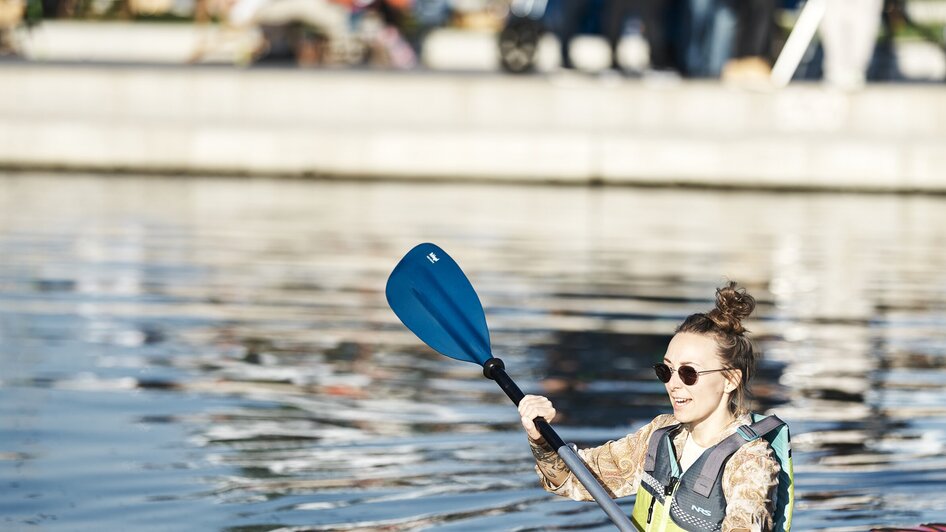Eine Person paddelt in einem Kajak am Stadtstrand in Graz.